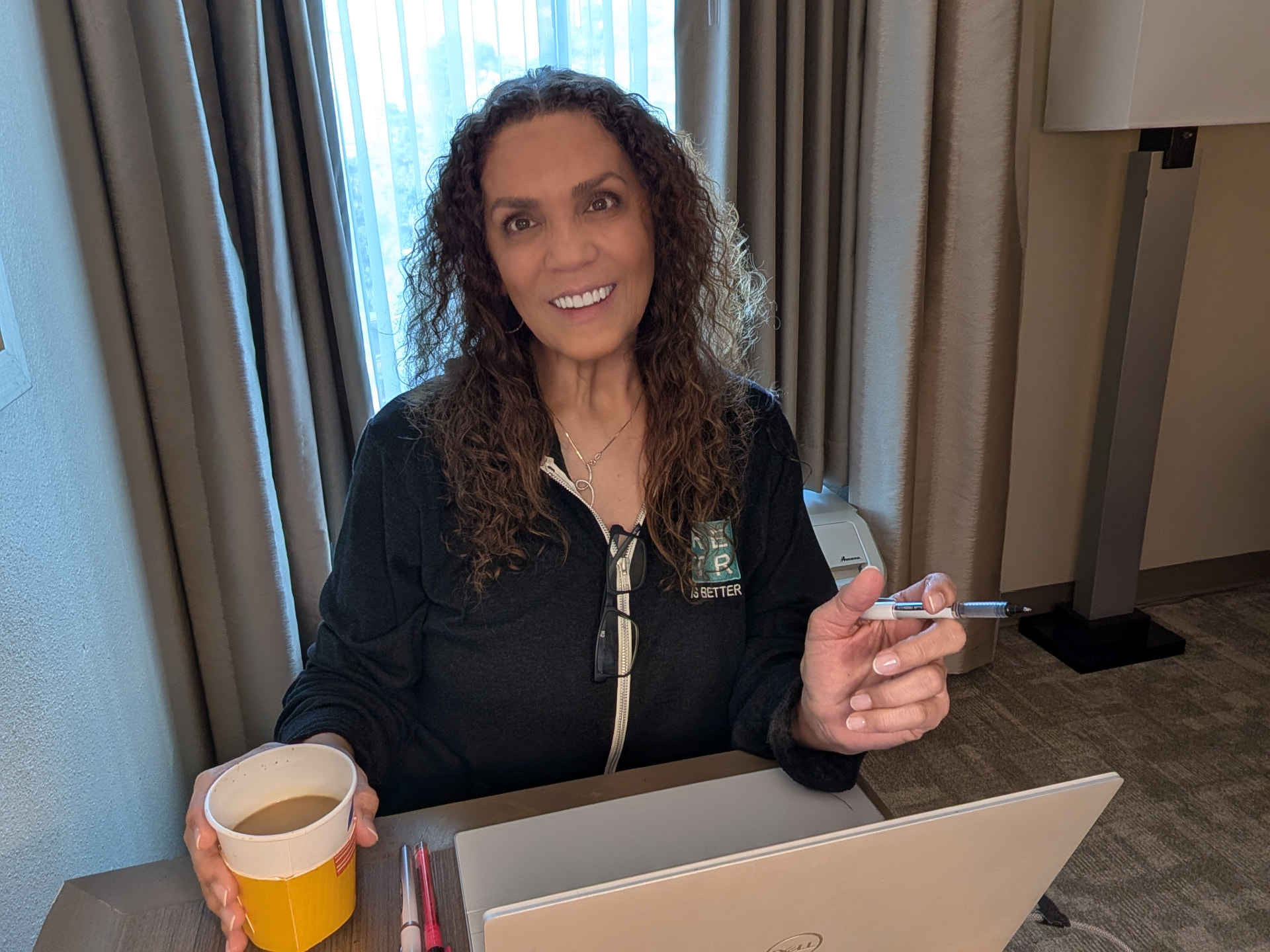Suha Beidas Zehl, CMB®, AMSP™ smiling at her desk with a coffee cup while writing